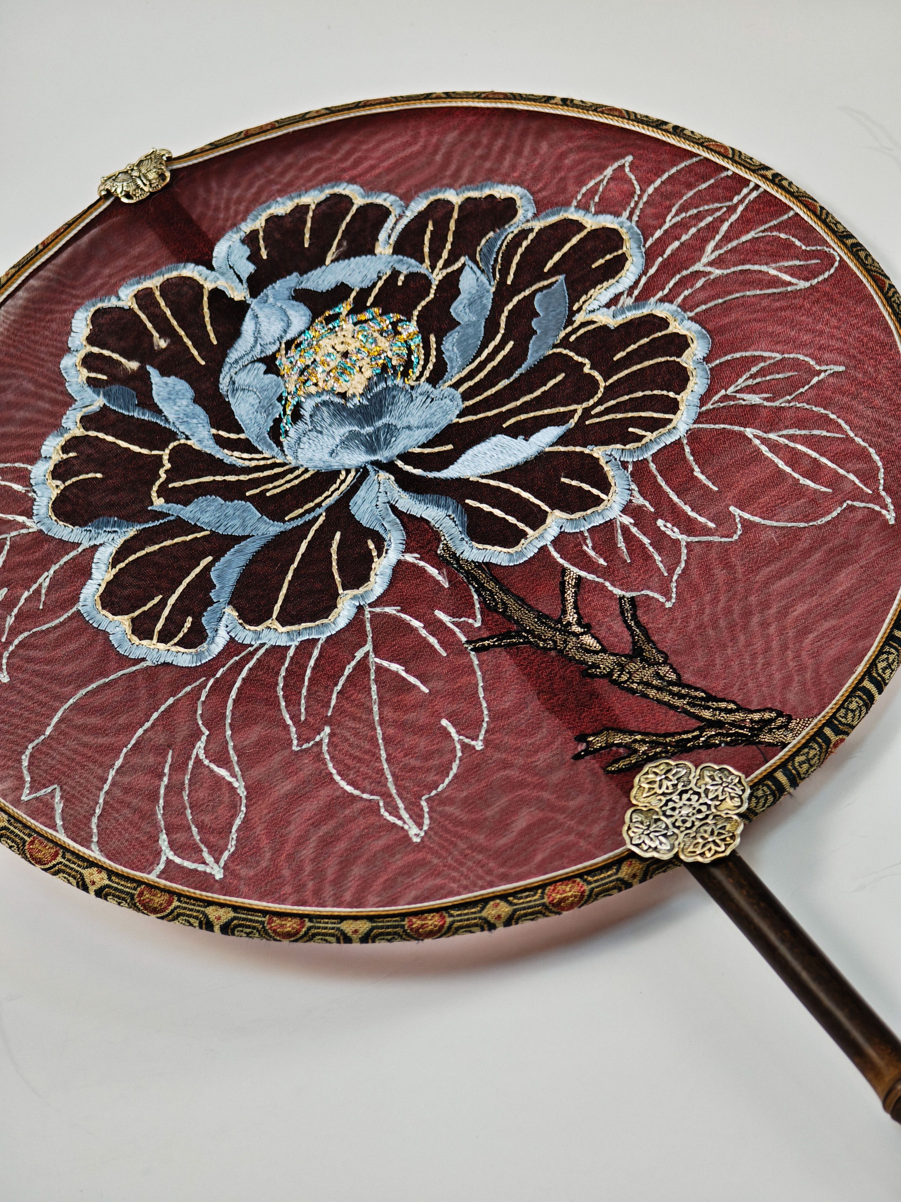 Silk embroidery surface with white leaf stitching and antique metal rim
